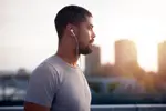 Man with earbuds pausing on a city rooftop at sunrise