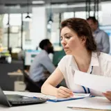 Woman at an office desk holding papers, looking focused